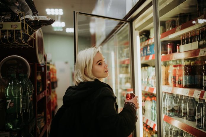 GS25 rice hotteok Korean convenience store snack - Blonde woman selecting a beverage from a refrigerated shelf at a convenience store.