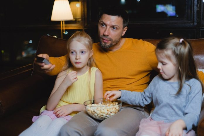 The Art of Sarah Netflix Korea top drama - A father and his two daughters enjoying a movie night with popcorn on the couch.